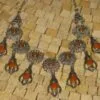 Ce collier en métal argenté, agrémentée de breloques en forme de fleurs et de pendentifs en pierre orange vif.